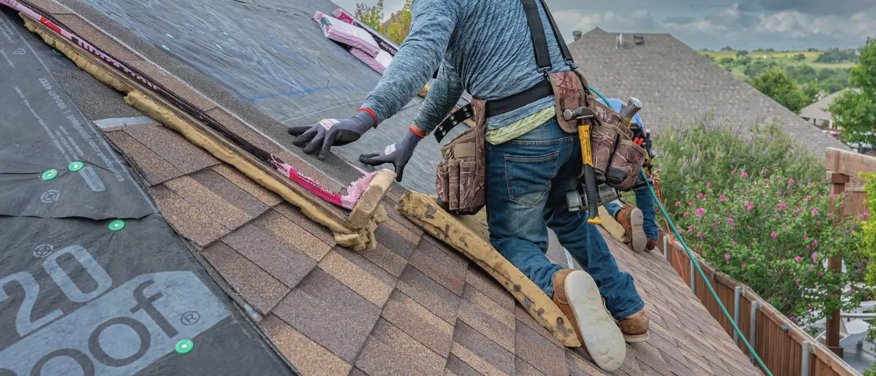 A roofer laying shingles on a house under a grey sky