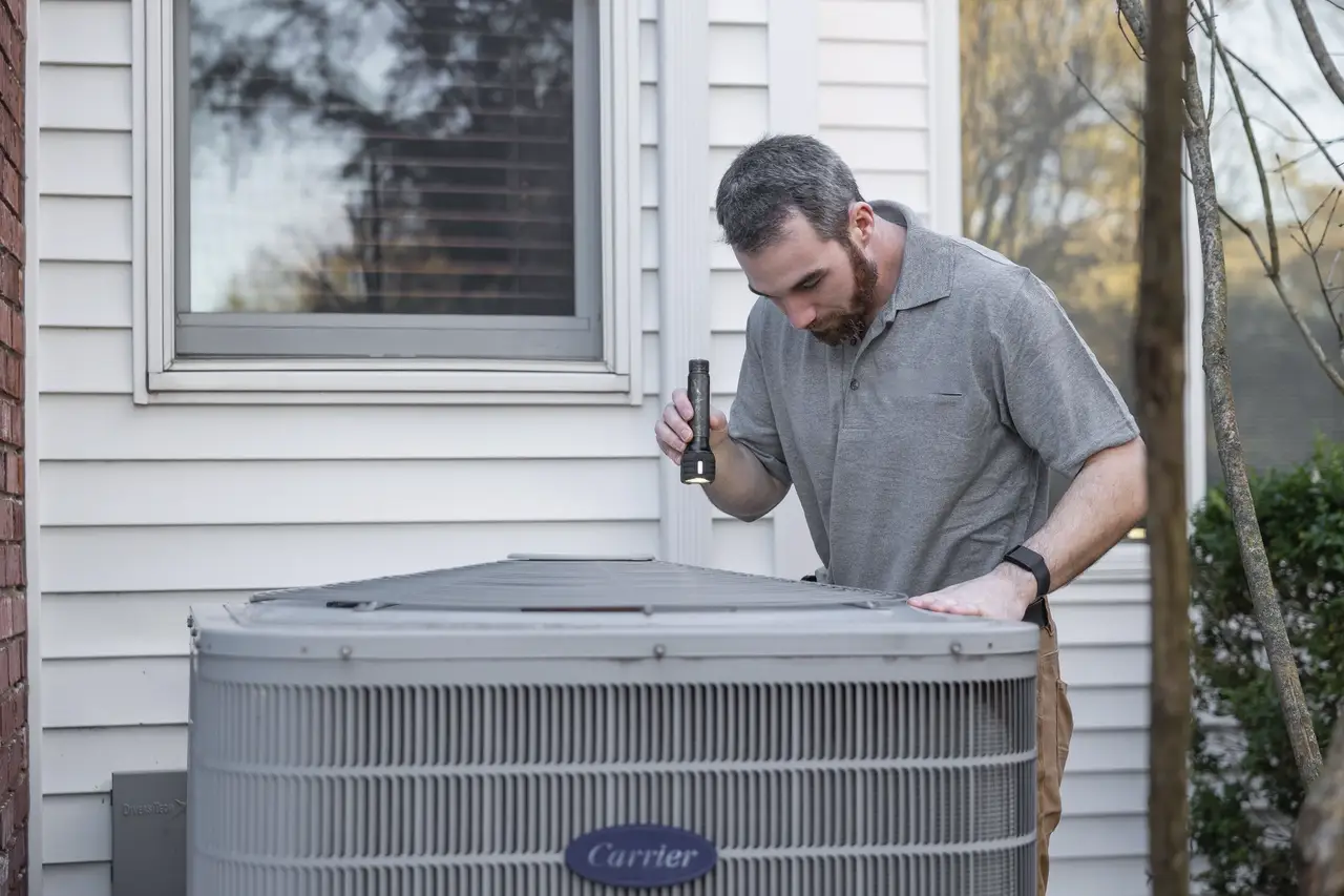 A technician checking an outdoor air conditioning unit beside a house