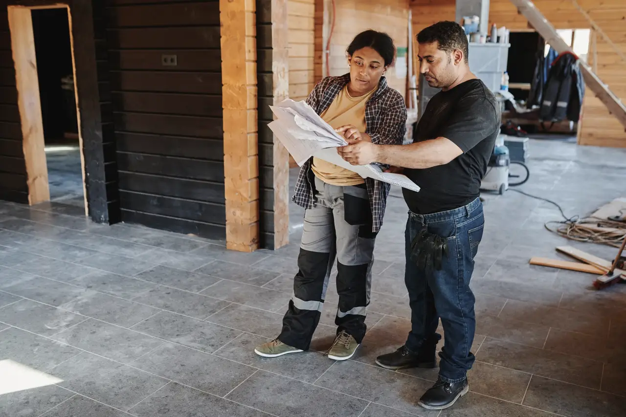 Two builders reviewing plans inside a timber-framed house under construction