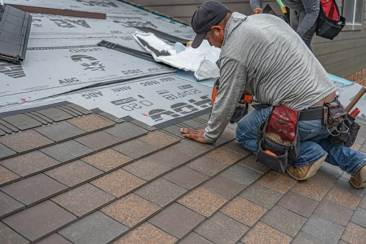 A roofer kneeling on a roof, nailing shingles